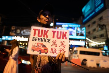 PHUKET, THAILAND - APRIL 15, 2023: a man hold tuk tuk service sign at Bangla Road, Patong Beach Walking Street. clipart