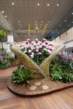 SINGAPORE - 25 AĞUSTOS 2024: Büyülü Bahçe 'de çiçekler, Changi Havalimanı, orkideler, heykel sanatı, dolambaçlı yollar, ve bir koi göleti, terminalin içinde huzurlu bir deneyim sunan.