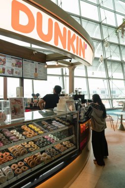 SINGAPORE - 25 AĞUSTOS 2024: Kadınlar Changi Uluslararası Havalimanı Terminal 2 'deki Dunkin' Donuts sayacındaki personelle etkileşim halindeler.