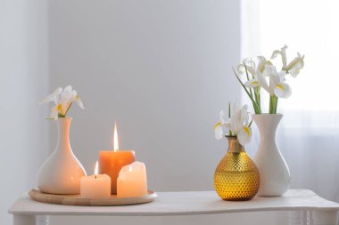 Beyaz iç kısımdaki ahşap rafta yanan mumlar ve bahar çiçekleri.