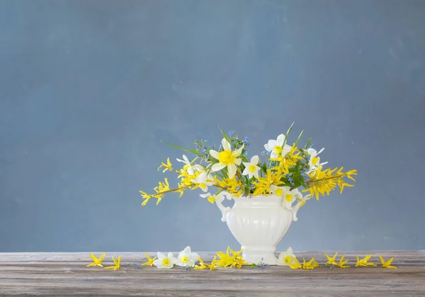 青い背景の木のテーブルの上の花瓶に白と黄色の春の花 — ストック写真