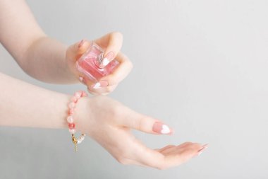 Beyaz arka planda parfüm şişesi olan kadın elleri