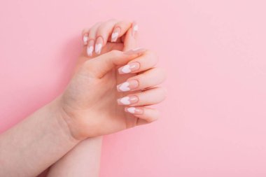 Güzel, uzun tırnaklı, manikürlü, pembe arka planda kalp deseni olan kadın elleri.