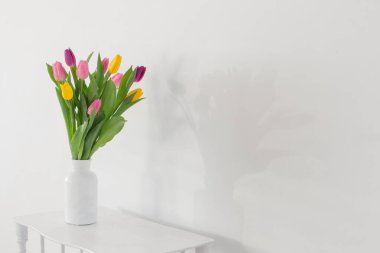 Beyaz arka plandaki ahşap rafta beyaz vazodaki laleler.