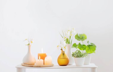 Beyaz iç kısımdaki ahşap rafta yanan mumlar ve bahar çiçekleri.