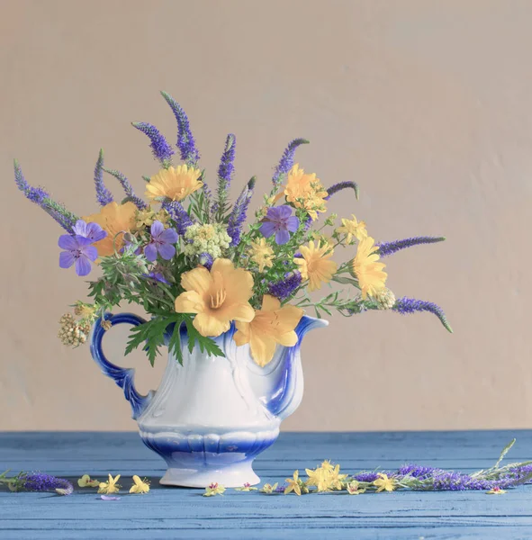 bouquet with blue and yellow flowers in teapot on wooden table