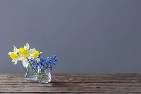 黑色背景的木制桌子上的花瓶里有黄色的水仙和蓝色的雪花 — 图库照片