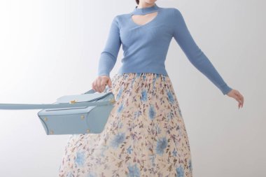 Mavi bluzlu, pileli etekli, beyaz arka planda mavi çantalı genç kız.