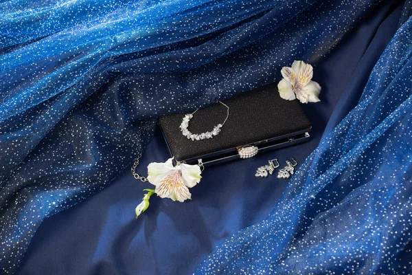 蓝色背景布上有珠宝的黑色离合器 — 图库照片