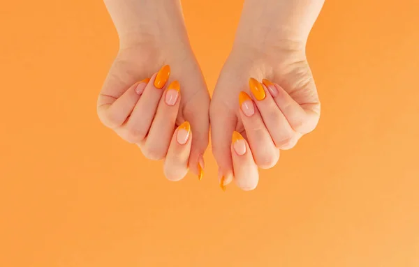 オレンジ色の背景にマニキュアを持つ女性の手 — ストック写真