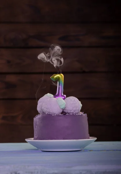 purple birthday cake with burning candle on wooden  background