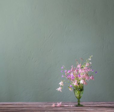 Arkadaki yeşil duvarda yeşil renkli çiçekler var.