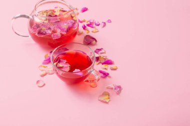 Pembe arka planda cam çaydanlıkta gül yapraklı çay