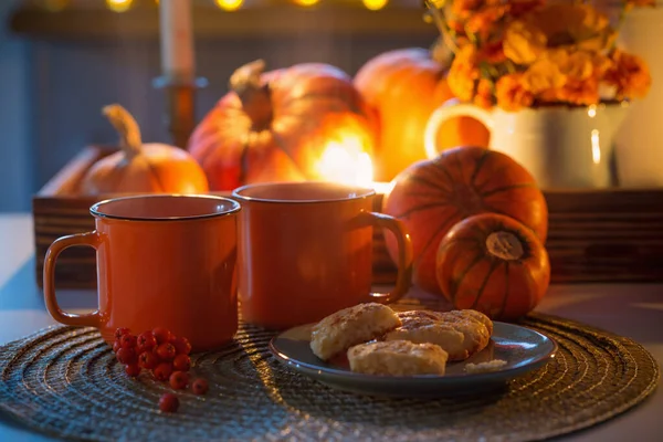 2つのオレンジティーカップとカボチャと秋の装飾花とテーブルの上の燃えるろうそく — ストック写真