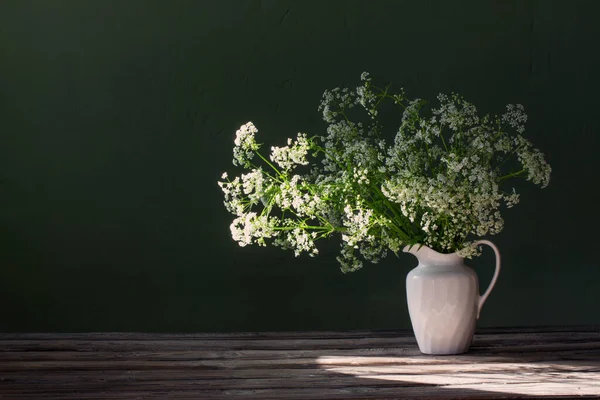 背景绿墙上的水壶中的白色野花 — 图库照片