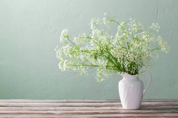 背景绿墙上的水壶中的白色野花 — 图库照片