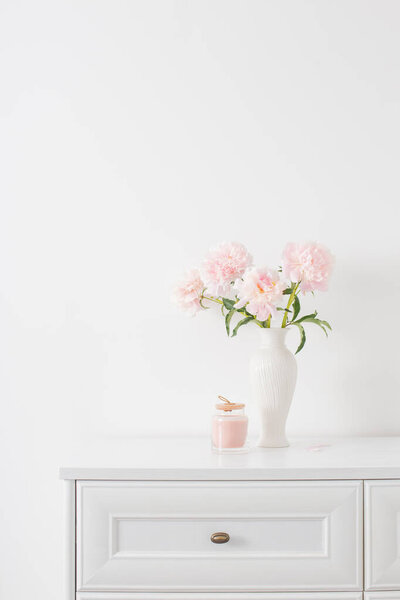 pink peonies in ceramic white vase in white interior