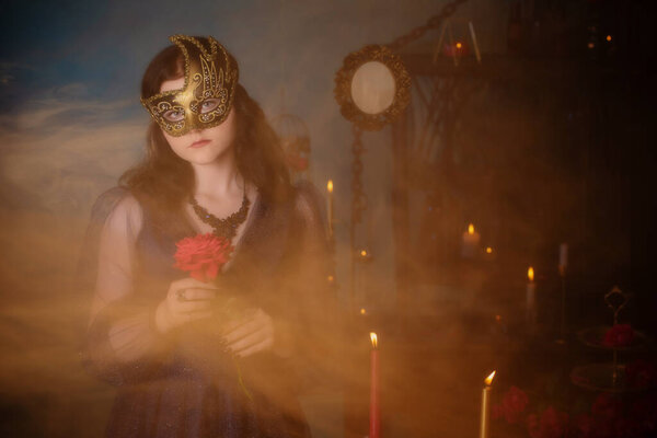 Young beautiful woman in golden mask and blue vintage dress in dark room