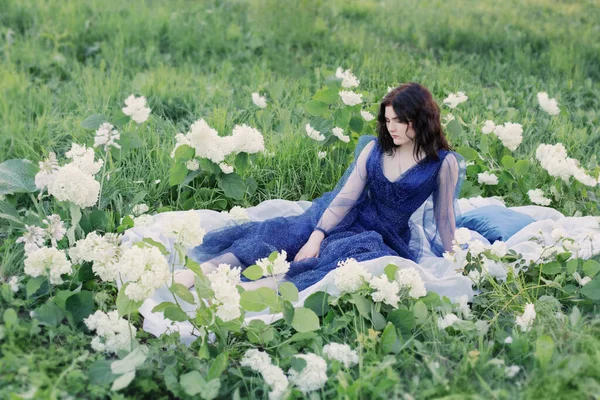 白い花を持つ草の上の青いドレスの若い美しい女性 — ストック写真