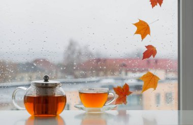 Pencere kenarında bir fincan çay ve pencere camında sonbahar yaprakları.