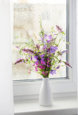 Beyaz pencere eşiğindeki yaz buketi yağmur damlaları