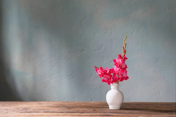 背景の青い壁に白い花瓶のピンクのグラジオラス — ストック写真