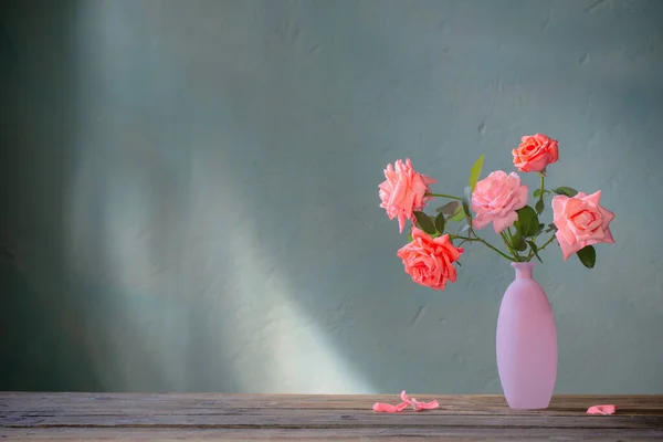 ピンクのバラのグラスピンクの花瓶の木のテーブルの上の背景暗い壁 — ストック写真