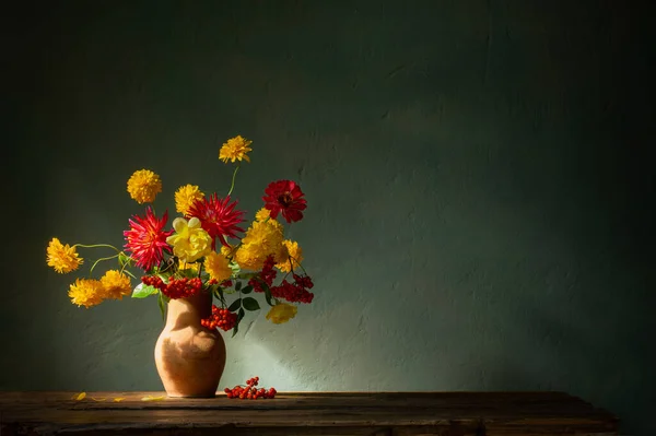 红色和黄色的花朵挂在水壶上 阳光照射在黑暗的墙壁上 — 图库照片