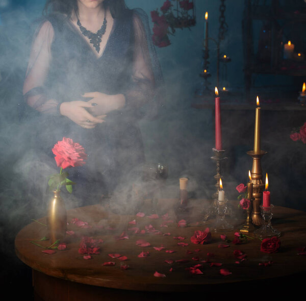 Young beautiful woman in blue vintage dress with red roses and magic potions in dark room