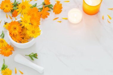 Beyaz mermer arka planda yanan mumlarla birlikte turuncu kadife çiçekleri.