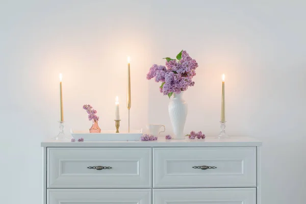 Lila Bloemen Witte Vaas Gouden Kaarsen Achtergrond Witte Muur — Stockfoto