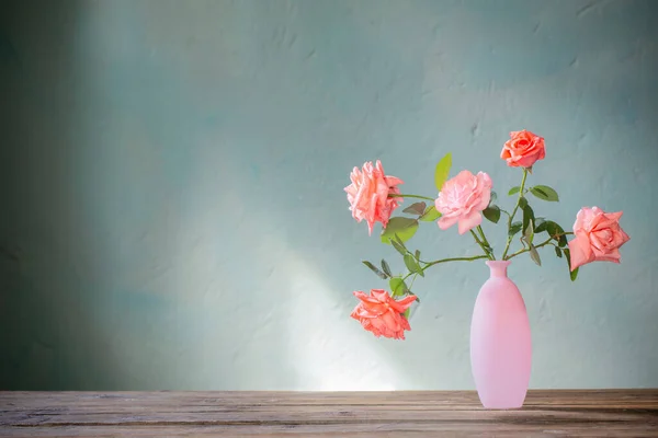 ピンクのバラのグラスピンクの花瓶の木のテーブルの上の背景暗い壁 — ストック写真