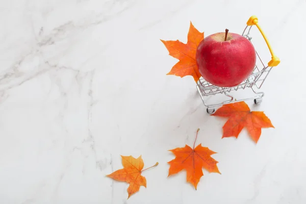 Czerwone Jabłko Małym Wózku Spożywczym Liści Klonu Białym Tle Marmuru — Zdjęcie stockowe