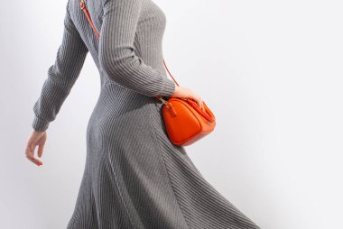 Beyaz arka planda turuncu çantalı gri formalı kadın.