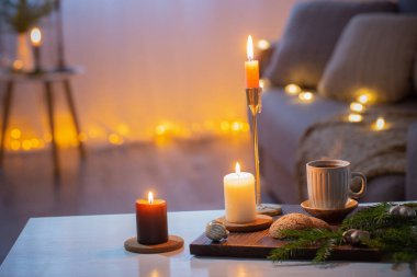 Evde yanan mumlar ve Noel süslemeleri olan bir fincan kahve.