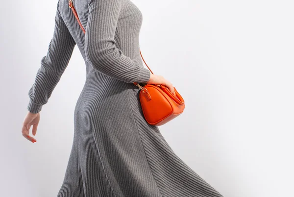 woman in gray jersey dress with orange handbag on white background