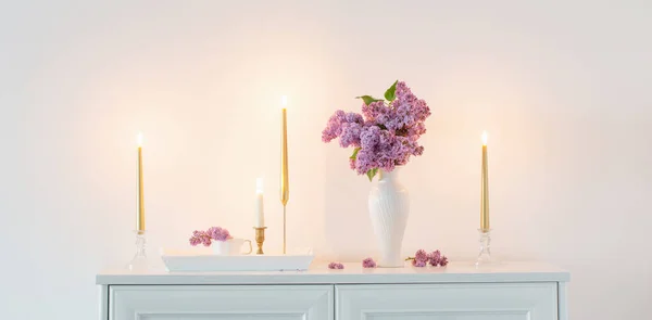 Lila Bloemen Witte Vaas Gouden Kaarsen Achtergrond Witte Muur — Stockfoto