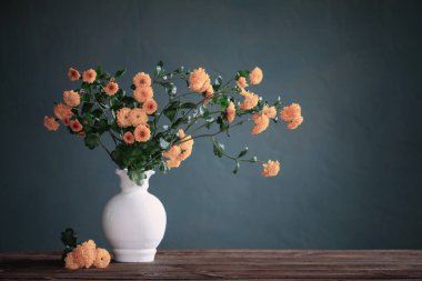 Beyaz vazoda sarı kasımpatılar. Arka plandaki siyah duvarda.