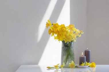 Sarı bahar nergisleri cam vazoda ve beyaz arka planda yanan mumlar.