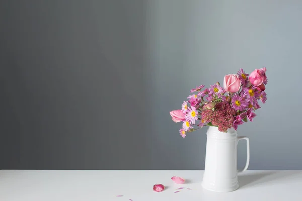 背景灰墙上白色水壶中的粉红花朵 — 图库照片