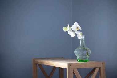 Beyaz orkide arka plandaki ahşap rafta duran klasik cam vazoda.