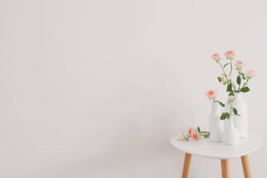 Arkadaki beyaz duvarda, beyaz vazoda pembe güller.