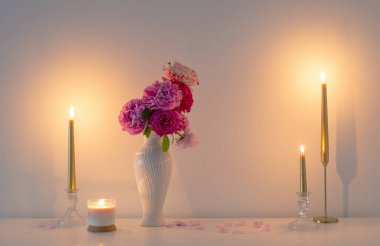 pink roses in vase and burning candle on background white wall clipart