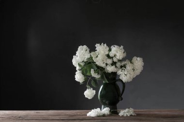 Beyaz hydragea, arka plandaki tahta masada antika sürahi içinde, karanlık duvarda.