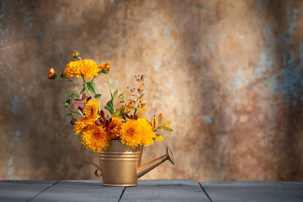 chrysanthemum flowers in golden watering can  on background old wall in sunlight