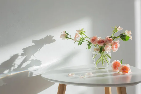 背景の白い現代的なテーブルの上のガラス瓶のピンクのバラ白い壁 — ストック写真