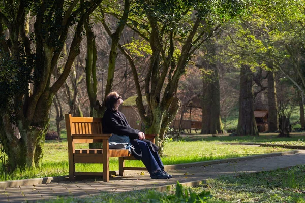 春の日当たりの良い公園の木のベンチにいた若い女性 — ストック写真