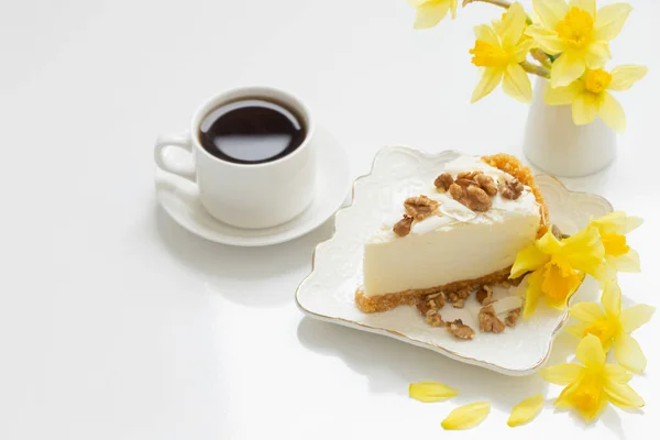 cheesecake with cup of coffee and yellow spring flowers on white table