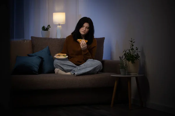 少女晚上在沙发上吃三明治 — 图库照片
