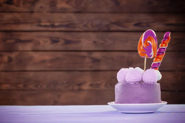 purple birthday cake with lollipops on dark wooden  background